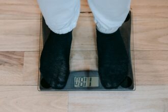 Henkilö seisoo digitaalisella henkilövaa'alla sukissa. Vaaka näyttää lukemaa 81 kilogrammaa. Kuvituskuva