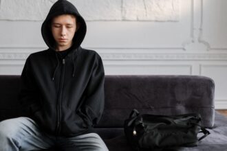 Kuvassa nuori mies istuu yksin sohvalla surullisen näköisenä. Kuvituskuva