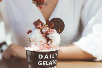 Nainen pitelee mansikkaa värikkään jäätelöannoksen yllä kahvilan pöydässä. Kuva: Michael Dagonakis / Unsplash