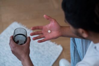 Henkilö pitelee tablettia kämmenellään ja vesilasia toisessa kädessään valmistautuessaan ottamaan lääkkeen. Kuva: Ron Lach / Pexels