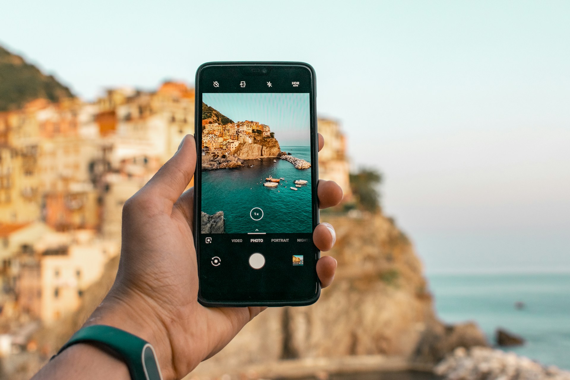 Matkailija kuvaa älypuhelimella Manarolan rannikkokylää Italiassa. Kuva: Dominik Dancs / Unsplash