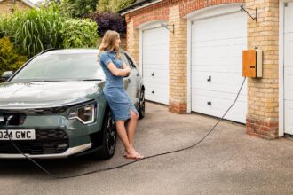 Nainen lataamssa kotinsa latauspisteestä sähköautoa