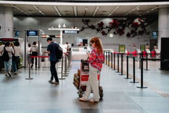 Matkustaja seisoo matkatavarakärryn vieressä lentoasemalla ja katsoo älypuhelintaan. Kuva: Dongfang Xiaowu / Pexels