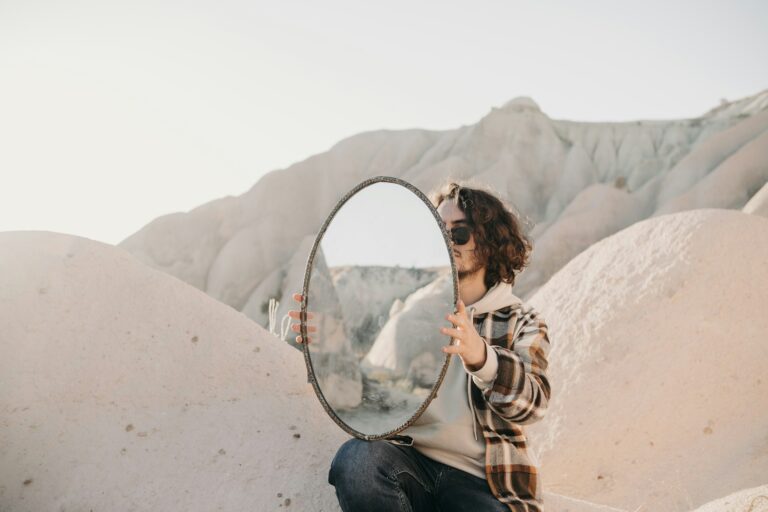 Mies aavikon dyyneillä polvillaan iso pyöreä peili polvella tuettuna- Kuva: Ali Ramazan Ciftci/Unsplash