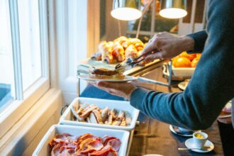 Hotellivieras kokoaa aamiaista runsaasta buffetista, jossa on lämpimiä ruokia, leivonnaisia ja hedelmiä.