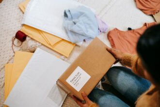 Henkilö pitää käsissään verkkokauppapakettia vaatteiden ja muiden postipakettien keskellä. Kuva: Liza Summer / Pexels