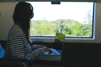 Henkilö työskentelee kannettavalla tietokoneella junassa kuulokkeet päässä. Kuva: Anna Shvets / Pexels. Kuvituskuva.