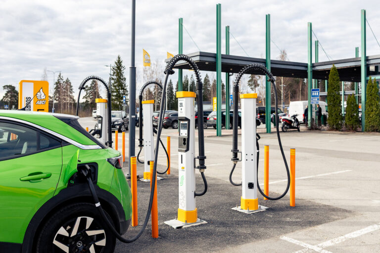 Vihreä sähköauto latauksessa ABC-latausasemalla. Kuvassa näkyy useita sähköautojen latauspylväitä, latauskaapeleita ja ABC-aseman tunnus. Kuva: Osuuskauppa Suur-Savo / STT Info