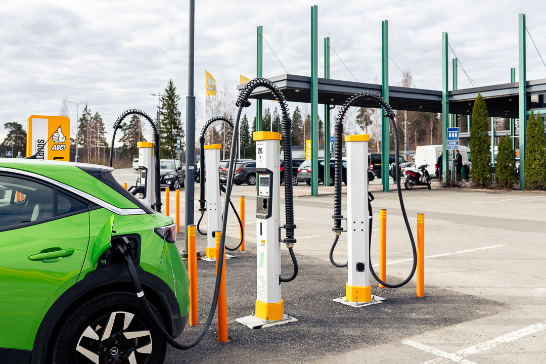 Vihreä sähköauto latauksessa ABC-latausasemalla. Kuvassa näkyy useita sähköautojen latauspylväitä, latauskaapeleita ja ABC-aseman tunnus. Kuva: Osuuskauppa Suur-Savo / STT Info