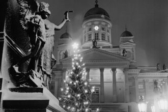Historiallinen mustavalkokuva Helsingin Senaatintorilta. Valaistu joulukuusi seisoo lumisten portaiden edessä, taustalla Helsingin tuomiokirkko ja vasemmalla suuri patsas.
