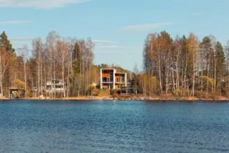 Moderni, suurilla ikkunoilla varustettu vapaa-ajan asunto suomalaisen järven rannalla metsän ympäröimänä.