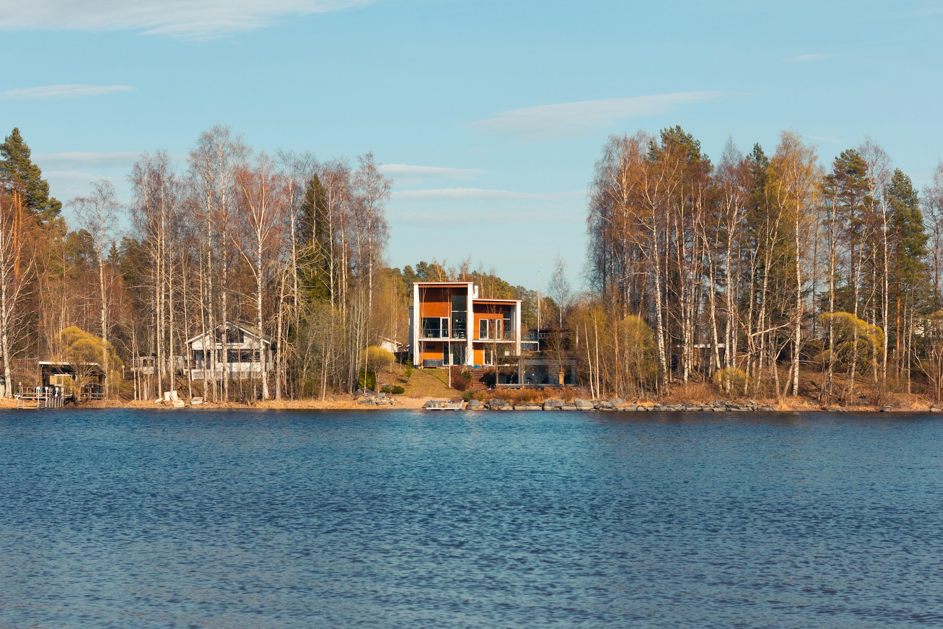 Moderni, suurilla ikkunoilla varustettu vapaa-ajan asunto suomalaisen järven rannalla metsän ympäröimänä.