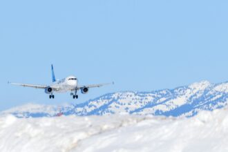 Matkustajakone laskeutumassa lumiselle lentokentälle vuorten ympäröimässä talvimaisemassa.